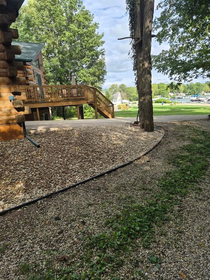 Pea gravel spread around a lakeside log home with a curved edging line around a mature tree.
