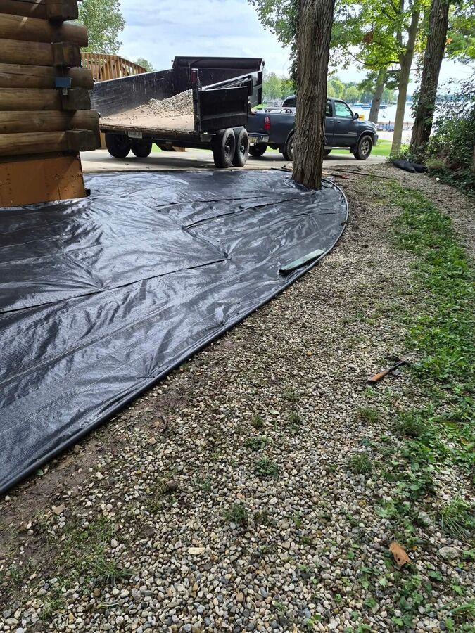 Black woven fabric fitted around a tree base with a dump trailer of crushed aggregate parked nearby.