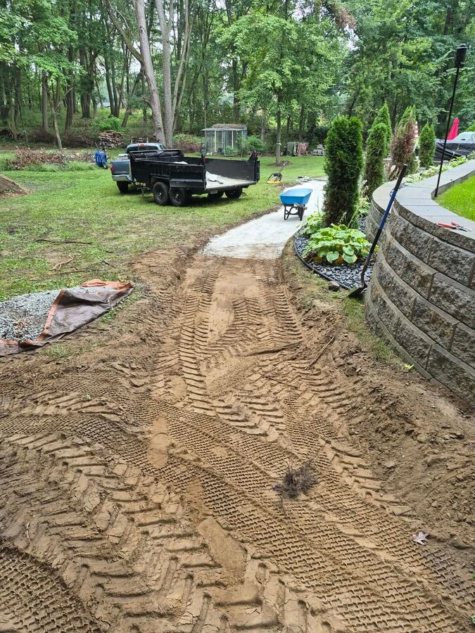 Curved path excavated beside a tiered stone retaining wall, with equipment and materials on site.